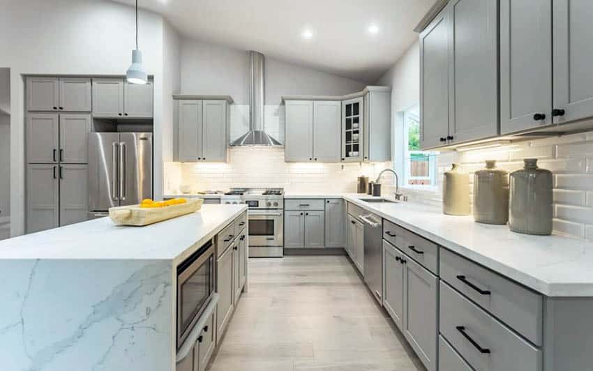 Beautiful kitchen with gray cabinets, quartz waterfall counter island and backsplash tile