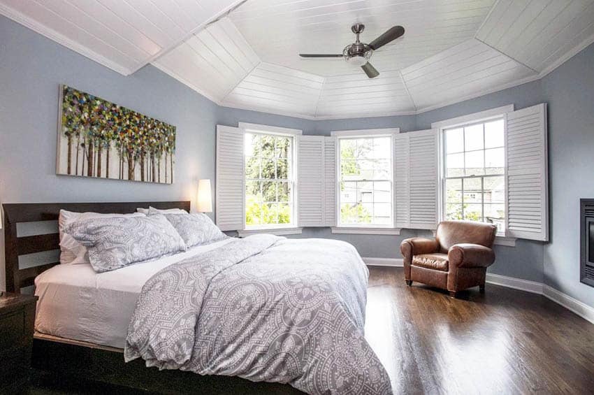 Bedroom with bed with brown headboard, tan leather chair and grey bedsheets