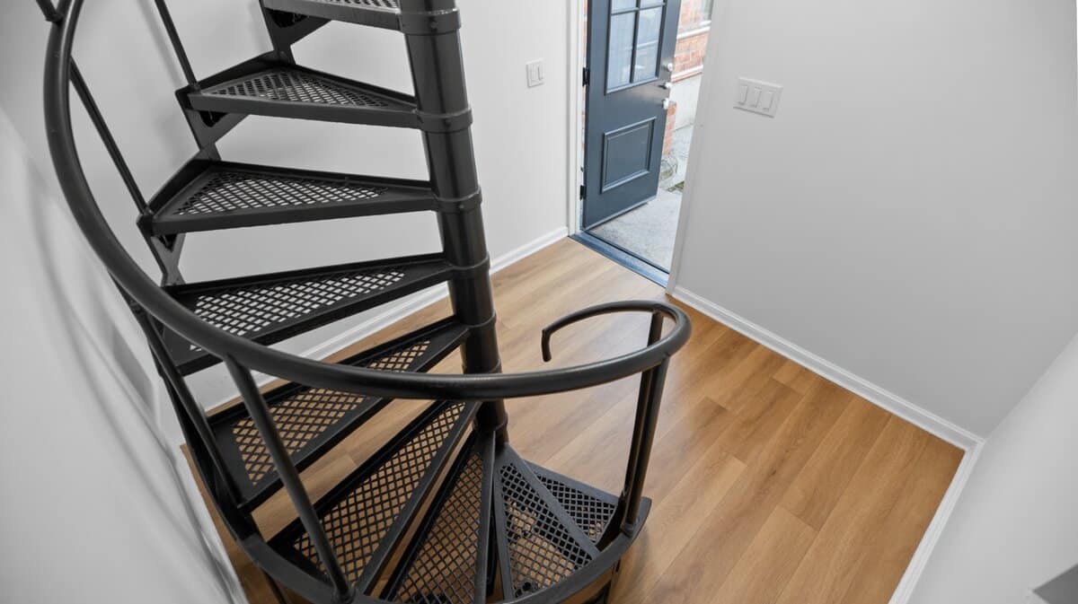 Black metal spiral staircase with diamond plate treads on natural oak laminate flooring