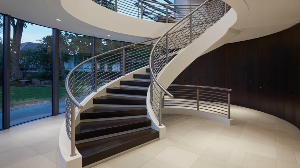 Contemporary curved spiral staircase with stainless steel horizontal railing and floor-to-ceiling windows with garden views