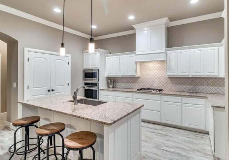 Kitchen with arabesque backsplash and white cabinets with beige granite island
