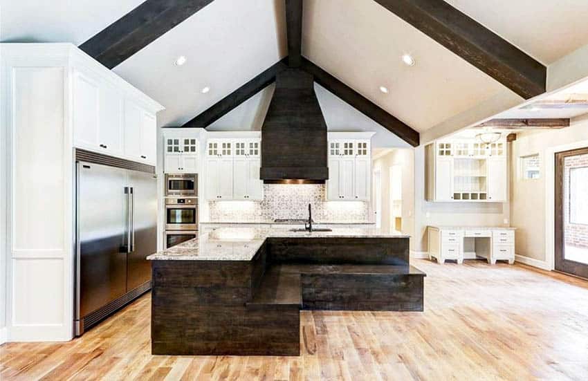 Kitchen with large faux wood beams, vaulted ceiling, white cabinets and built in bench seating island