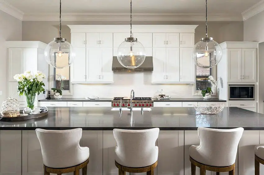 Kitchen with white cabinets and black quartz countertops, and globe pendant lights over island