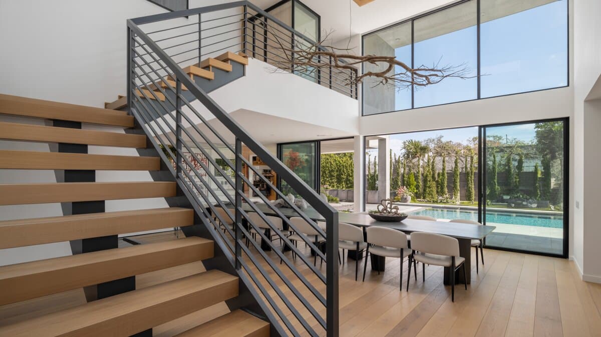Modern floating staircase with black horizontal metal railing opening to great room with pool views