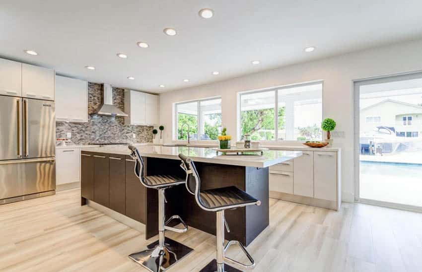 Kitchen with recessed lighting, glass tile backsplash, black island with stationary bar chairs