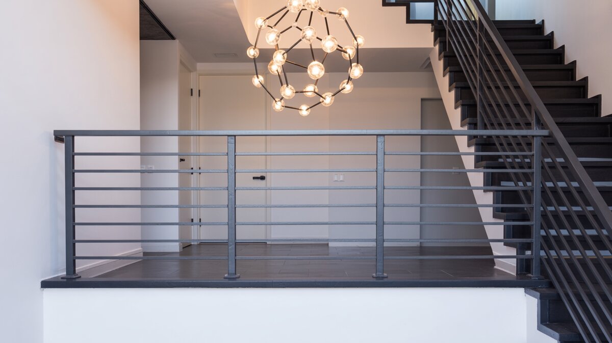 Modern stair landing with sleek horizontal black metal railing and sculptural molecular glass globe chandelier