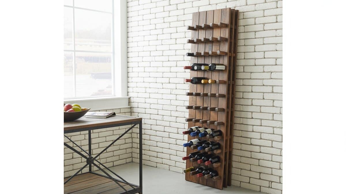Tall rustic wood vertical wine rack with wine bottles stored horizontally against a white brick wall