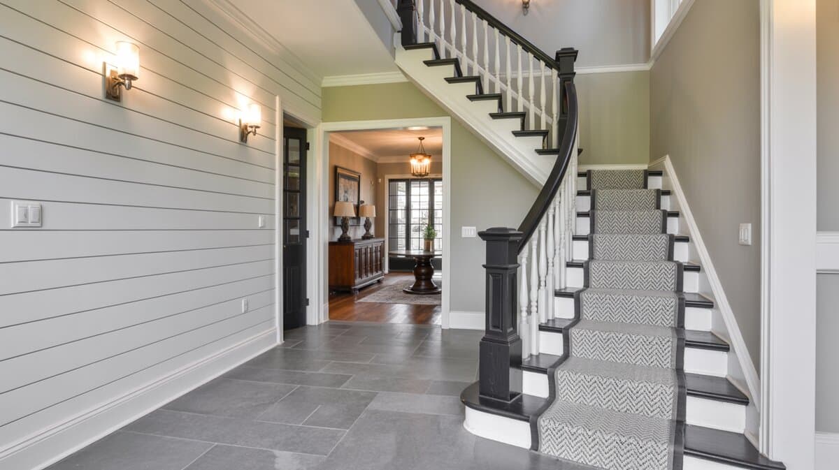 Transitional style foyer staircase with black handrail and white balusters on herringbone patterned carpet runner