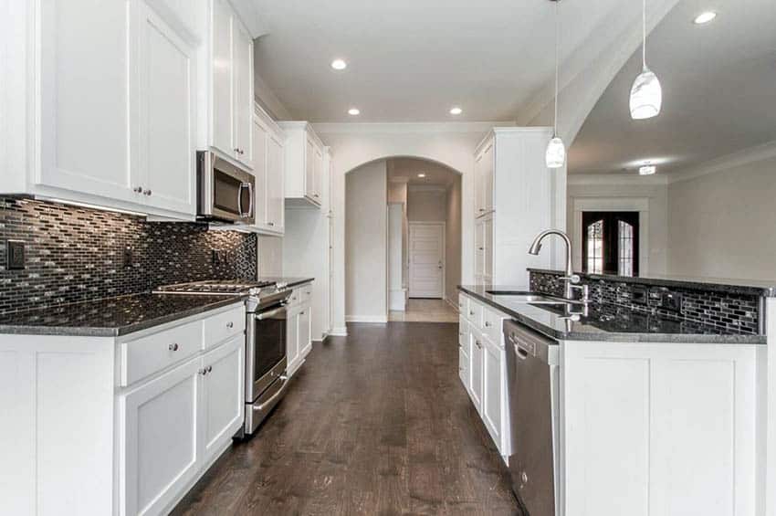 White open galley kitchen layout, black stone countertops and mosaic backsplash