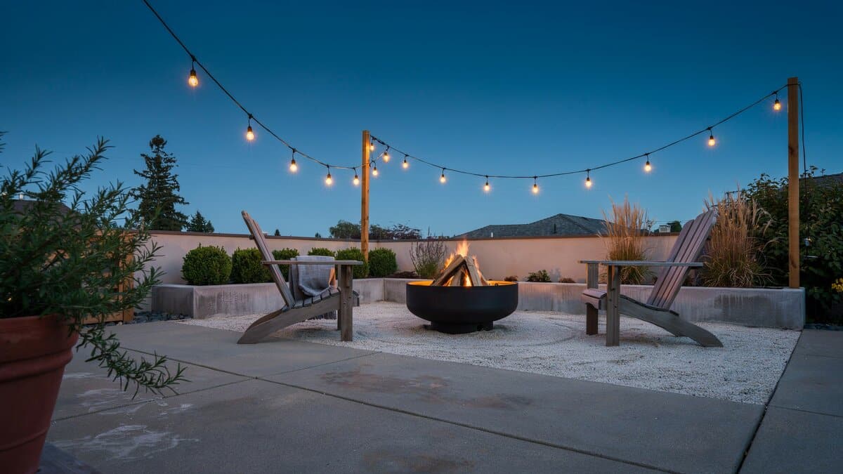 Gravel fire pit area with Adirondack chairs and lights along the wall