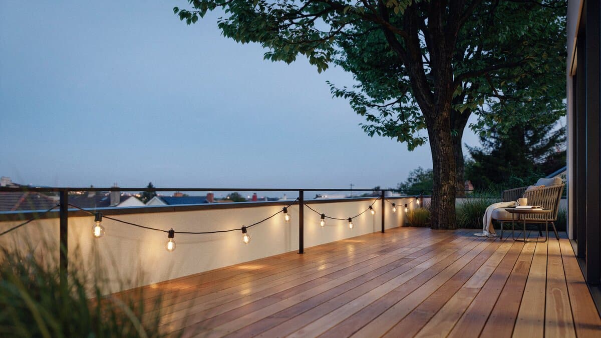 Wood deck with bulb lights along the railing beside a tall shade tree