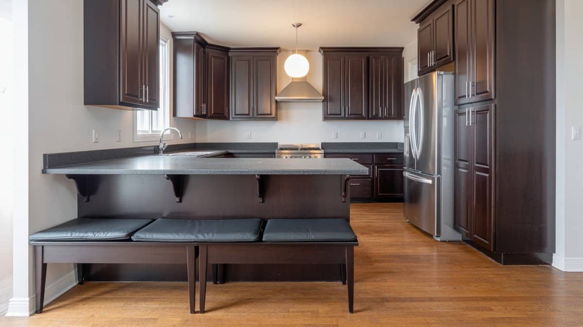 Dark espresso kitchen with granite peninsula and dark wood bench with cushioned seats attached to the counter