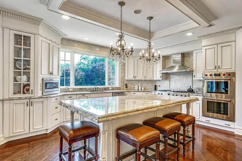 Kitchen with white backsplash and cabinets and beige brown countertops with two chandeliers