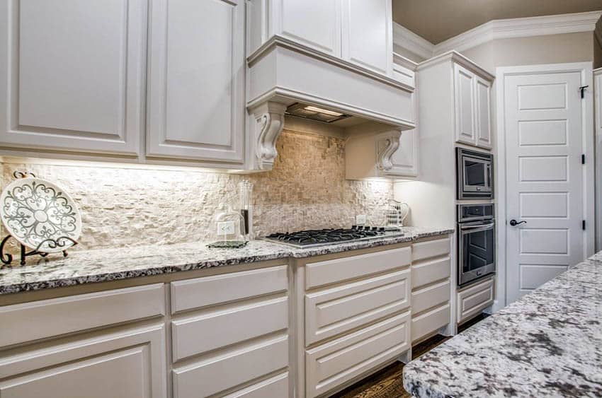 Kitchen with stacked stone backsplash white cabinets and white granite countertops