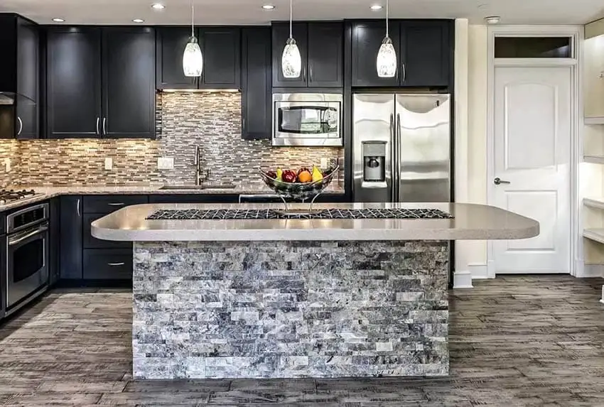 Kitchen with stone veneer base, white pendant lights and natural stone floors