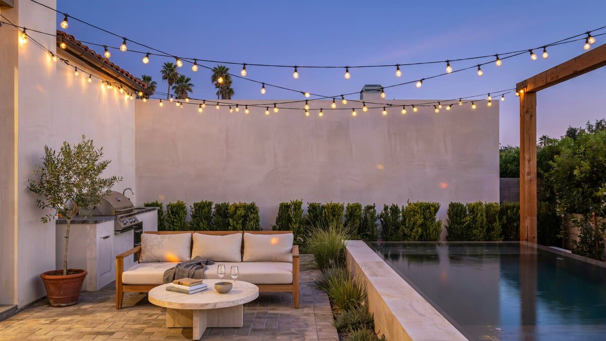 Warm lights attached to white stucco walls around a luxury pool patio
