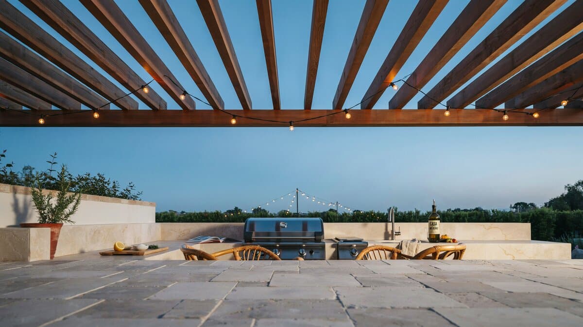 Outdoor kitchen counter beneath a slatted pergola strung with cafe lights