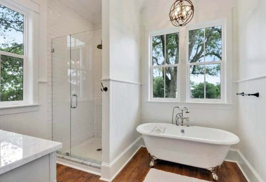 Traditional bathroom with small walk in shower beadboard wainscoting wood flooring and claw foot tub