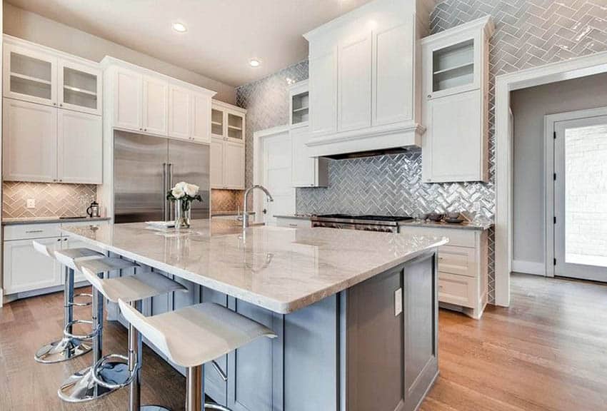 Kitchen with gray porcelain tile backsplash in herringbone pattern with white cabinets marble countertops and gray island