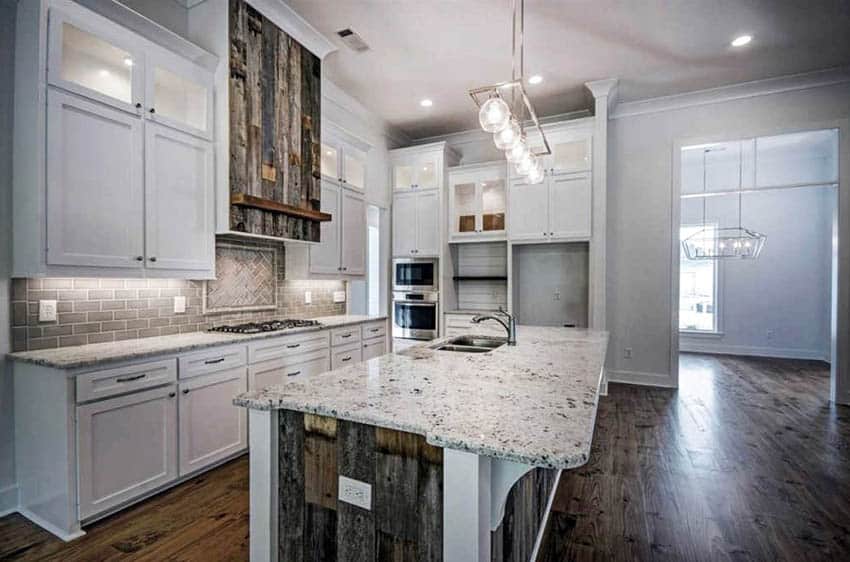 Kitchen with reclaimed wood island, hood, white cupboards and gray subway tile backsplash