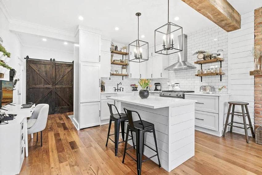 Beautiful kitchen with cabinetry in bright white, shiplap surround island, wood beam ceiling, sliding barn doors and open wooden shelving