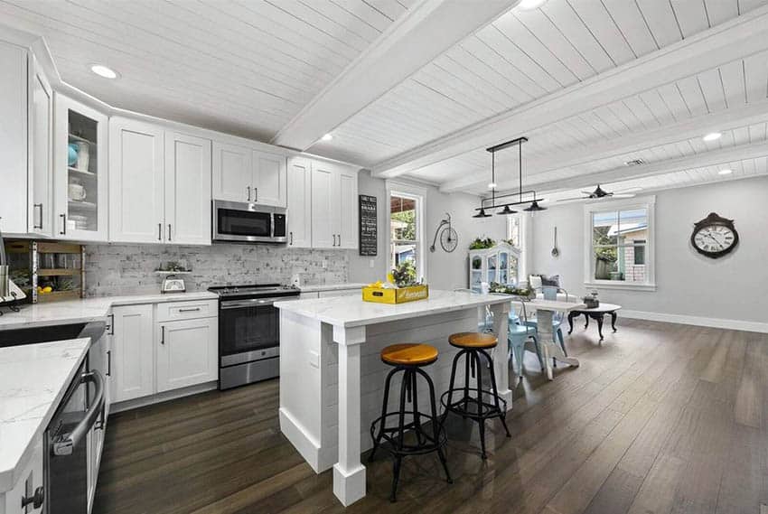 Kitchen with ceiling boards and pillar legged island, white cabinets and dark wood flooring