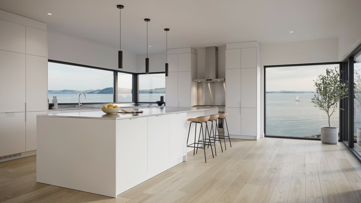White island topped with stainless steel beside wraparound windows framing a bay view