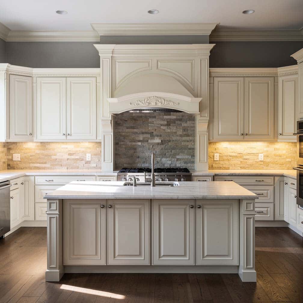 Antique white raised panel cabinets with grey walls and a floor-to-ceiling architrave with arched pelmet over the range hood