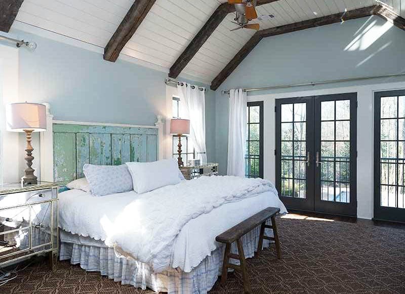Cottage master bedroom with french doors wood beams and distressed wood bed headboard