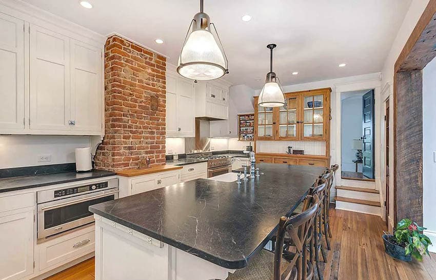 Kitchen with black soapstone counters with white cabinets, wood floors and brick accent wall