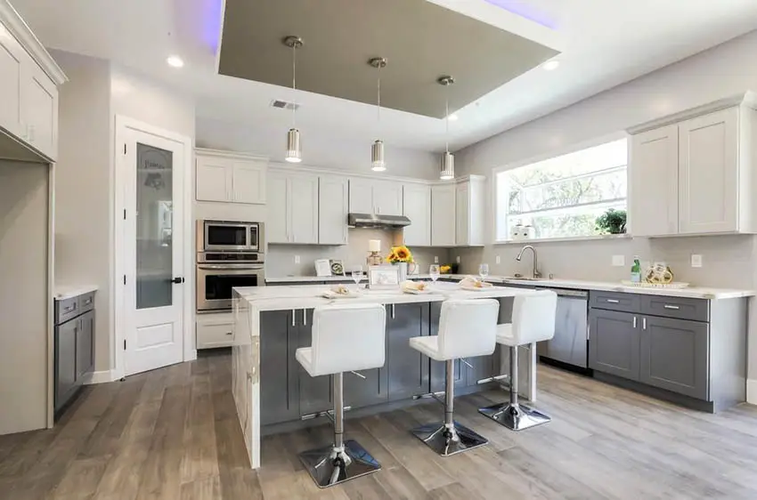 Kitchen with reverse tray ceiling with neon lights, white cabinets, gray island and quartz countertop