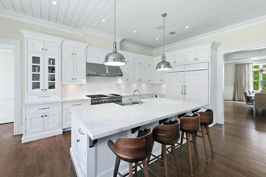 Kitchen with white cabinets, white marble countertops, tile backsplash and wood flooring