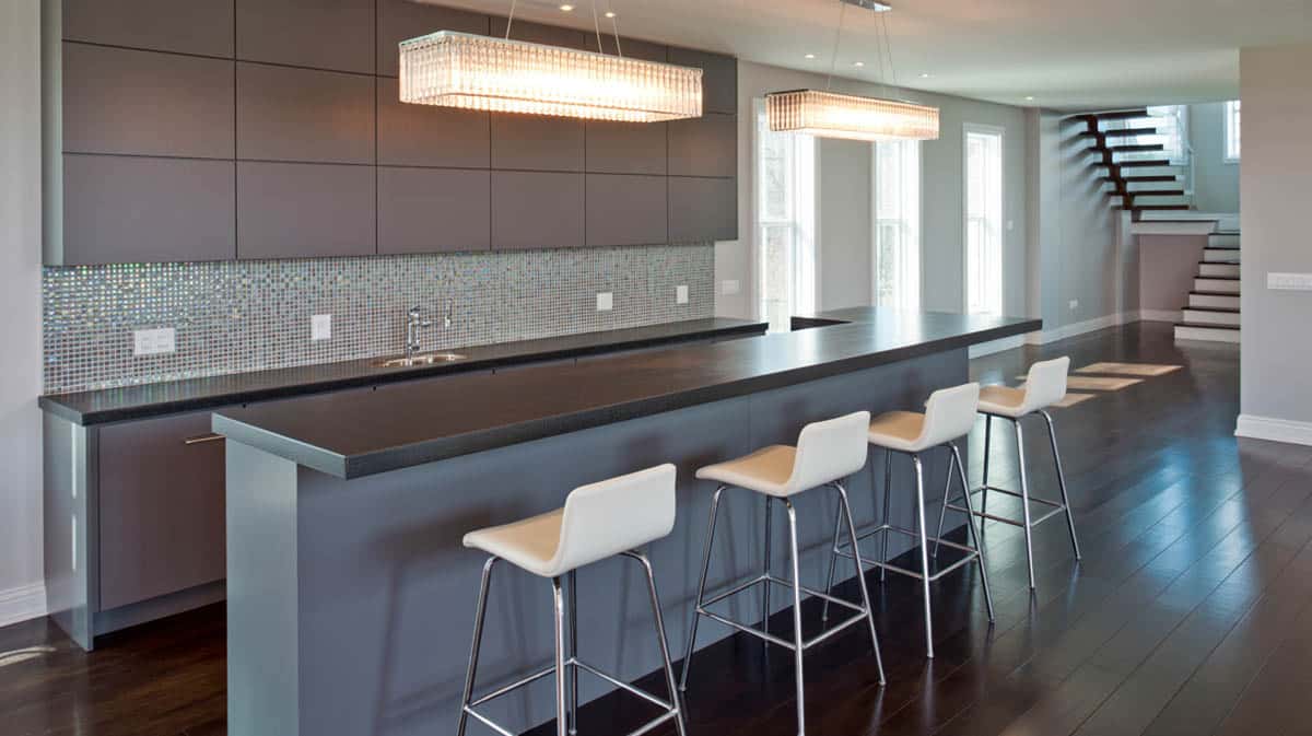 Minimalist bar with dark brown and gray tones, leather stools, and a mosaic tile backsplash