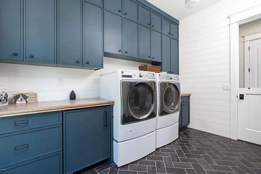 Blue painted laundry cabinets with gray herringbone tile flooring.