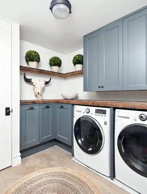 Small laundry with blue cabinets wood shelving and plants