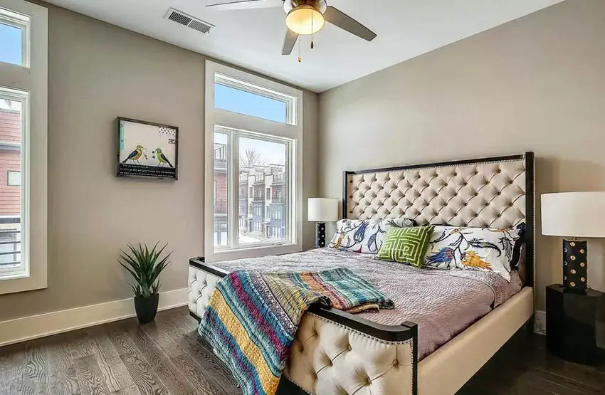 Cream walls, a ceiling fan and multicolored sheet on top of beige bed