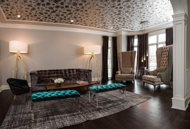 Living room with brown tufted sofa, teal ottomans, wallpaper ceiling and wood flooring