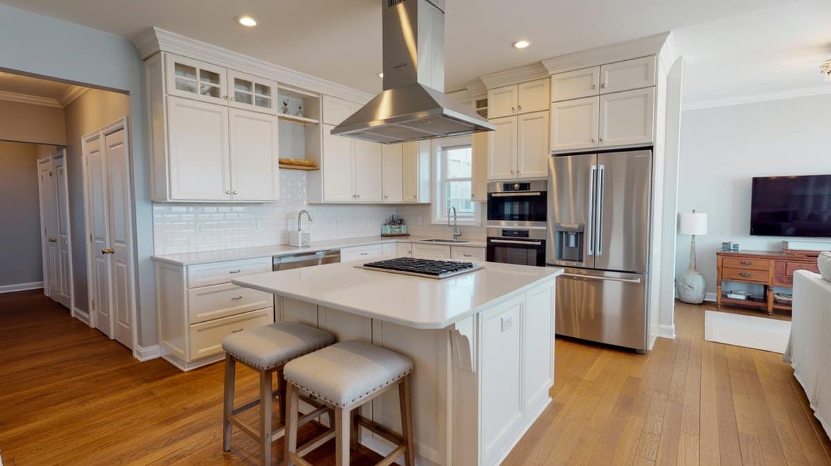 Open plan white kitchen with ceiling-mounted stainless island hood and upholstered bar stools