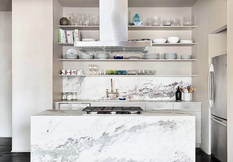 Contemporary kitchen with white cabinets quartz waterfall island and open shelving with glassware dishes