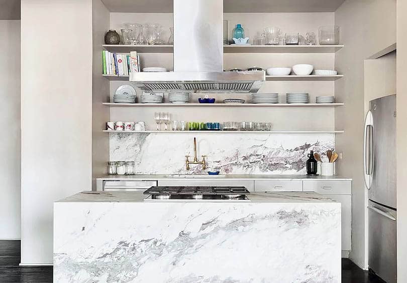 Waterfall marble island, stacked dishes, refrigerator and white walls