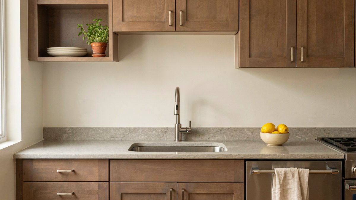 Wood kitchen cabinets with a short granite backsplash and a plain painted wall above
