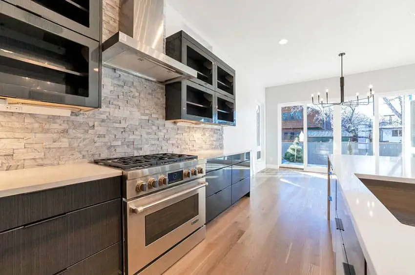 Kitchen with doorless black cabinets, stacked stone backsplash and wood flooring