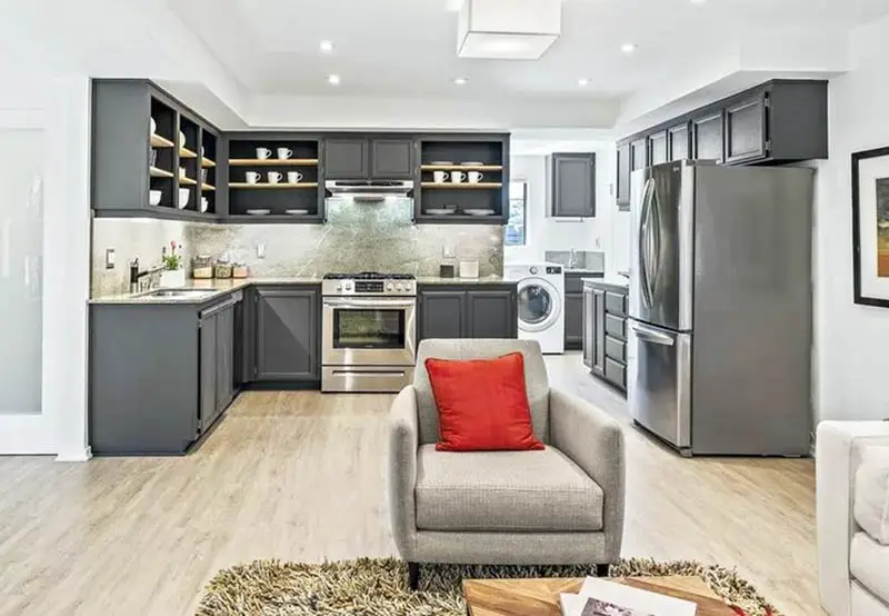 Kitchen with cabinets with no doors and couch with red pillow