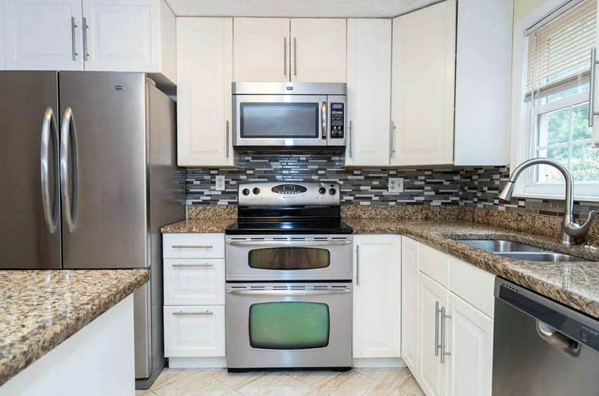 Kitchen with two types of contrasting backsplash, white cabinets and beige granite countertops