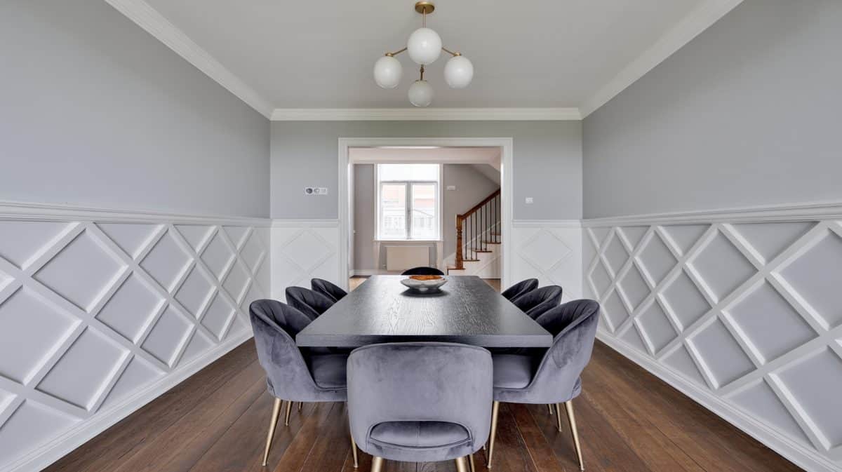 Dining room with white diamond-pattern geometric Art Deco panels on gray walls, long black dining table, gray velvet chairs, and globe cluster chandelier