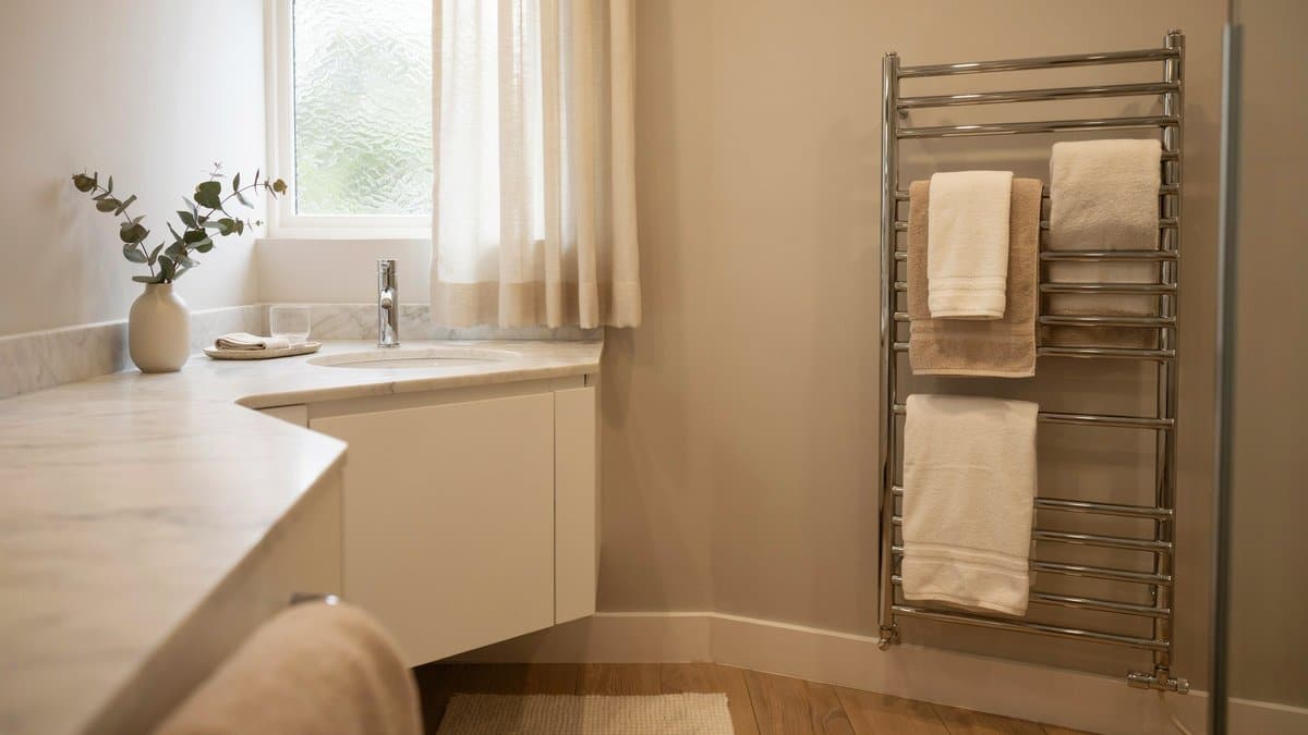 Tall chrome towel warmer on a warm neutral wall across from a marble vanity