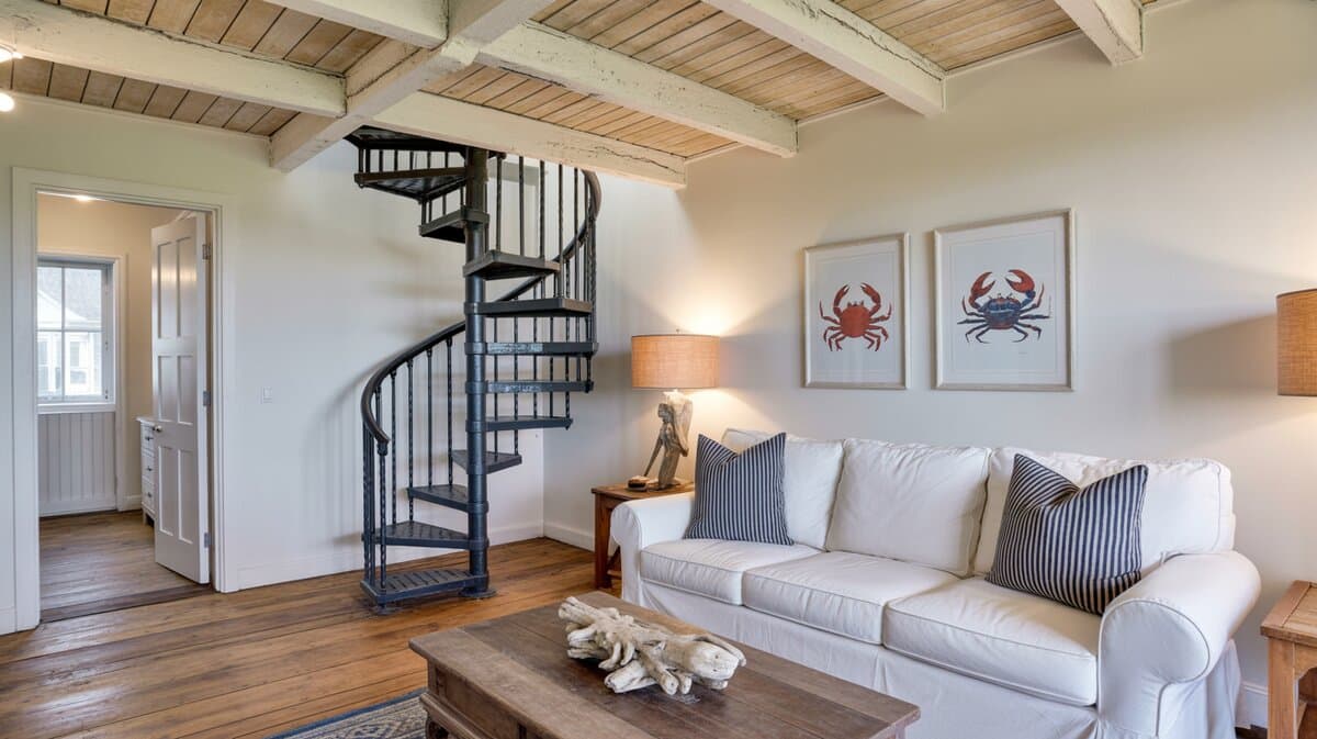 Coastal cottage living room with black metal spiral staircase under timber beam ceiling with nautical decor