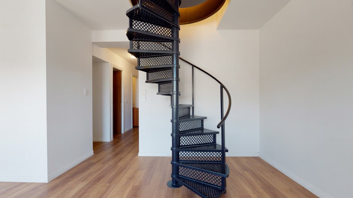 Compact black steel spiral staircase with perforated steps in residential hallway