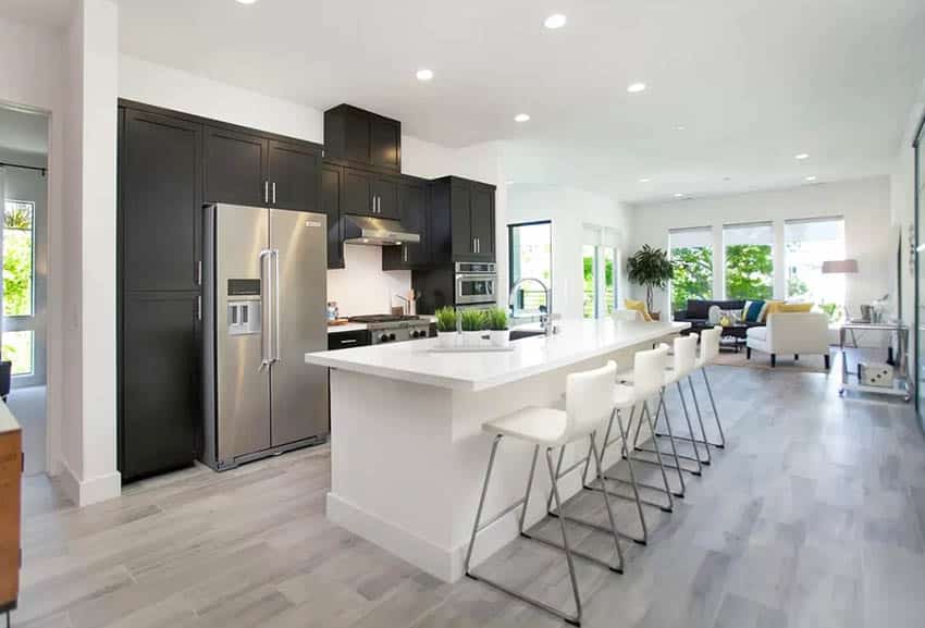 Contemporary kitchen with gray wood look porcelain tile flooring, black cabinets and white island