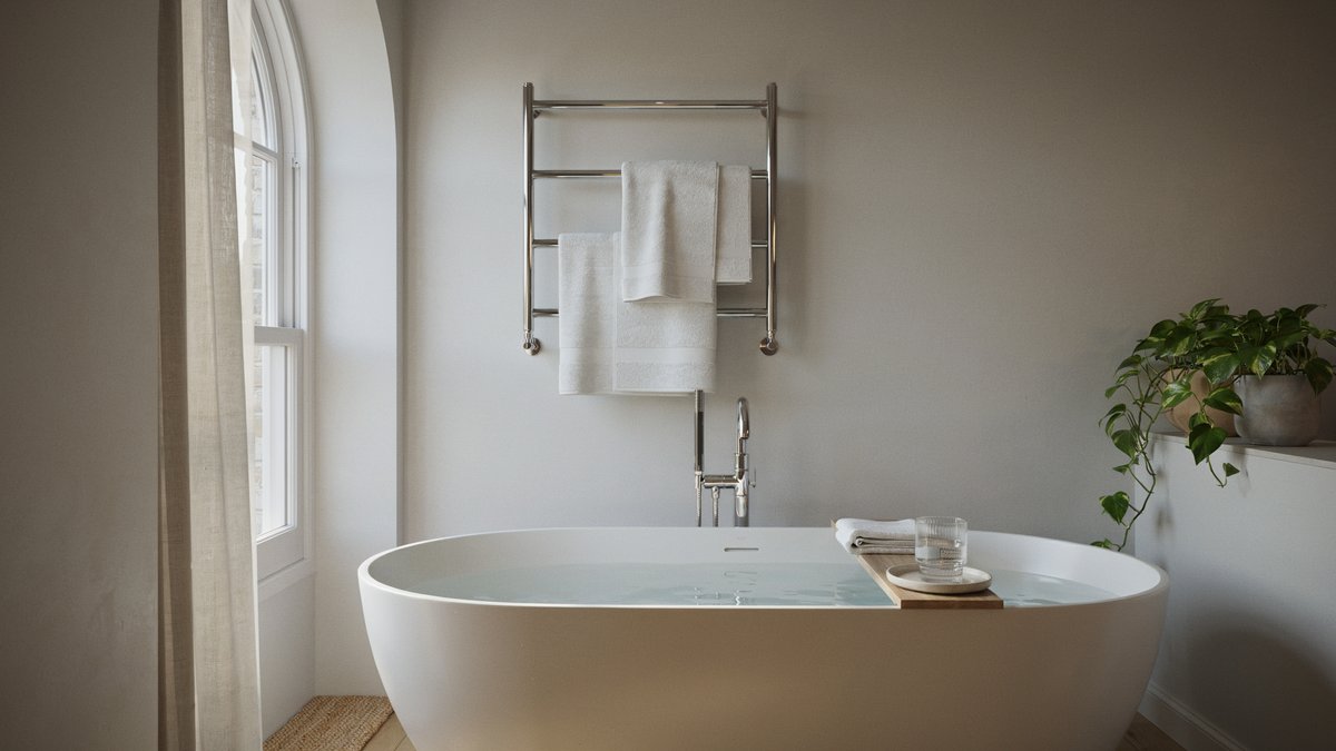 Chrome heated towel rail mounted above a freestanding oval tub with folded white towels